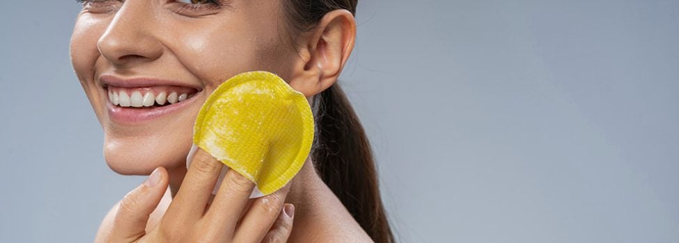 Close up portrait of a merry young woman performing an exfoliation procedure with a facial sponge